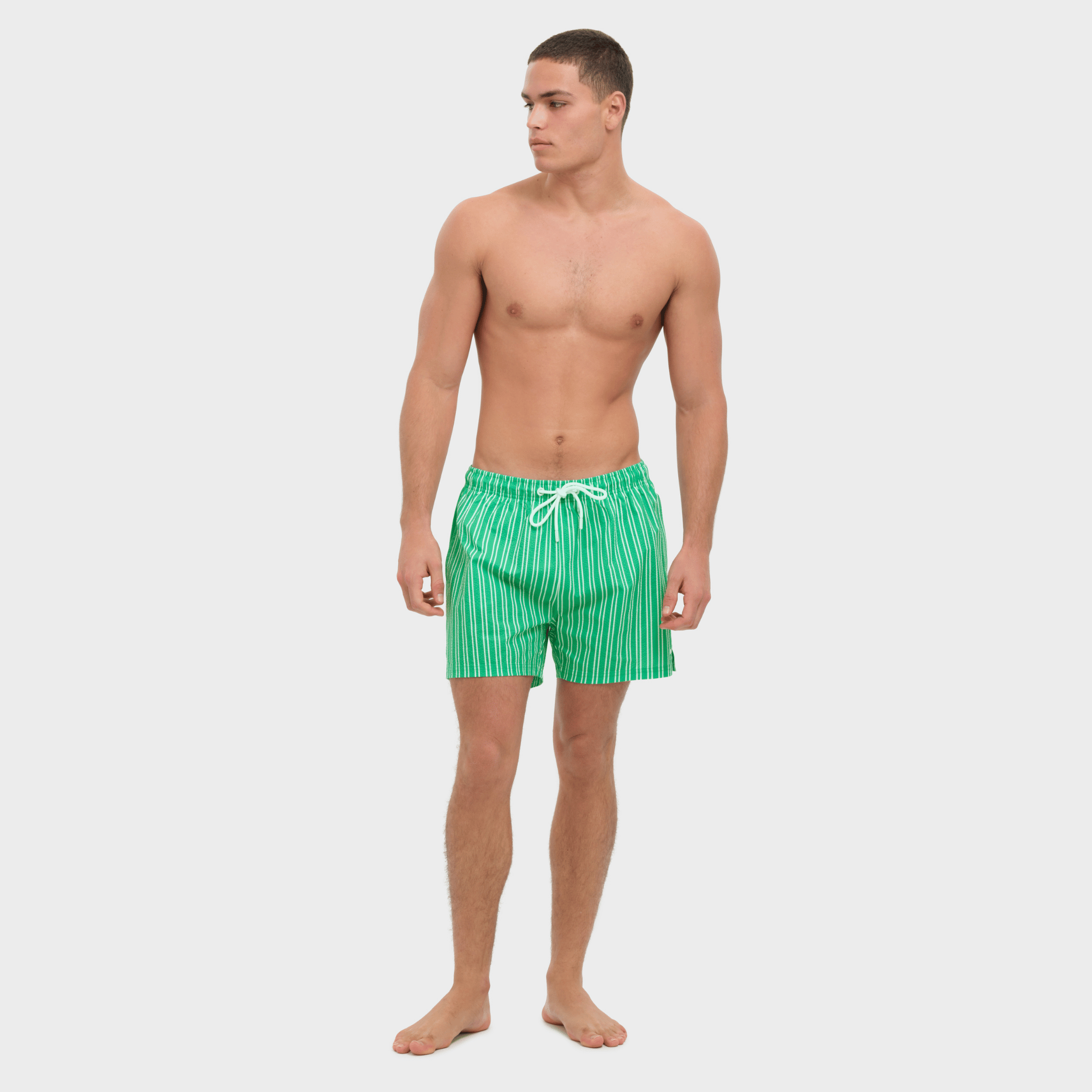 Man wearing green striped swim shorts on a white background