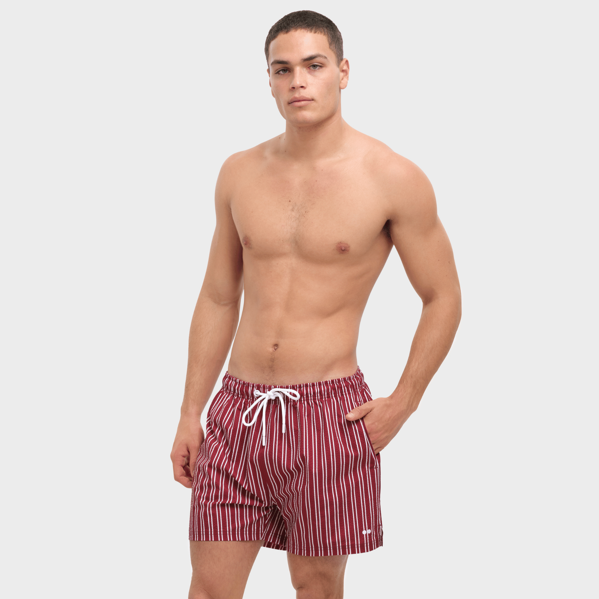 Man wearing red and white striped swim shorts on a plain background