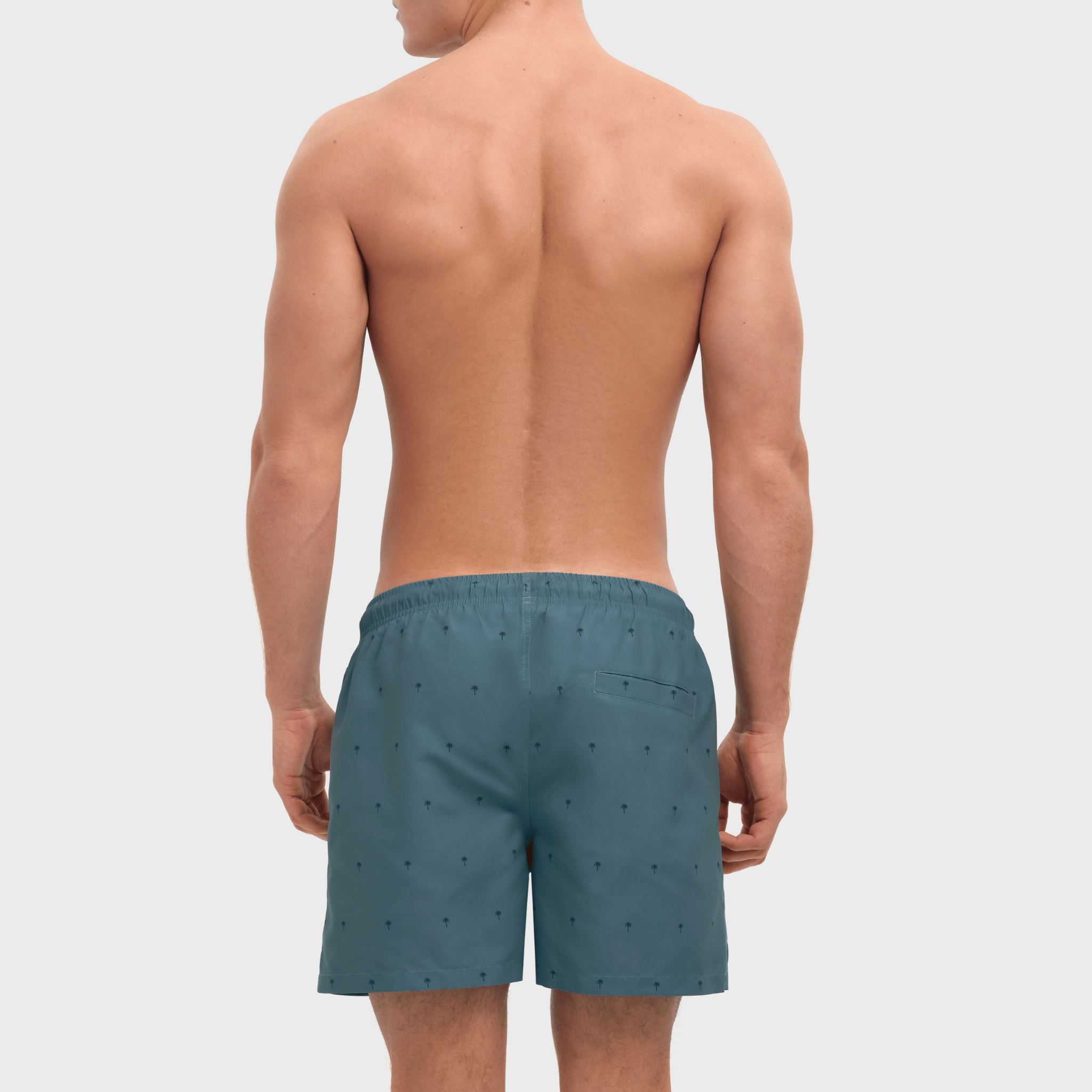 Man wearing teal swim shorts with a subtle pattern on a light gray background