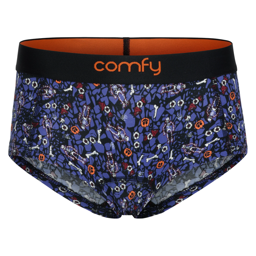 fit:hipster | quantity:1x | A pair of women's hipsters by Comfy featuring a dark blue and black Halloween-themed print with bones, ghosts, and jack-o'-lanterns, a black waistband with orange interior lining, and the brand name 'comfy' in orange on the front.