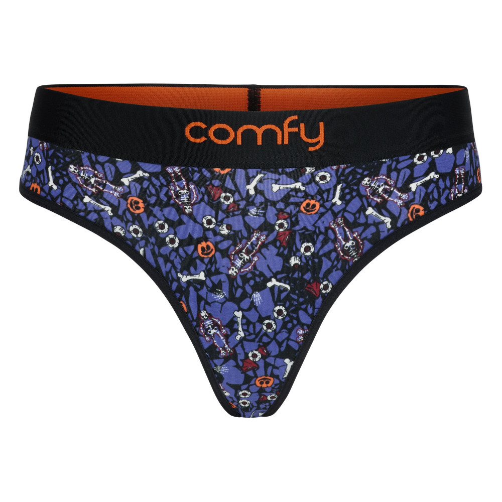 fit:string | quantity:1x | A pair of women's thong-style underwear by Comfy, featuring a dark blue and black Halloween-themed pattern with bones, ghosts, and jack-o'-lanterns, a black waistband with orange interior lining, and the brand name 'comfy' in orange on the front.