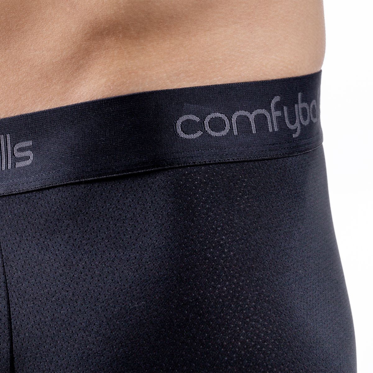 Close-up of a person wearing black mesh boxer briefs with a black elastic waistband featuring the visible brand name 'comfyballs' in light gray.