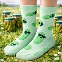 Green socks with pickle design worn by a person in a field with jars of pickles.
