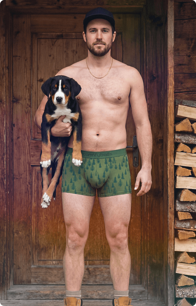 Man holding a puppy wearing green patterned underwear in a rustic setting
